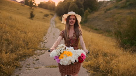 Ein-Glückliches-Und-Fröhliches-Mädchen-Mit-Hut-Fährt-Fahrrad-In-Einem-Kleid-Mit-Blumen-Auf-Dem-Feld-Und-Lächelt-Und-Genießt-Den-Sommer-Und-Die-Freiheit